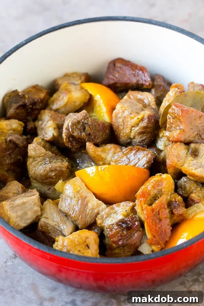 Cooked pork carnitas in a red pot with oranges.