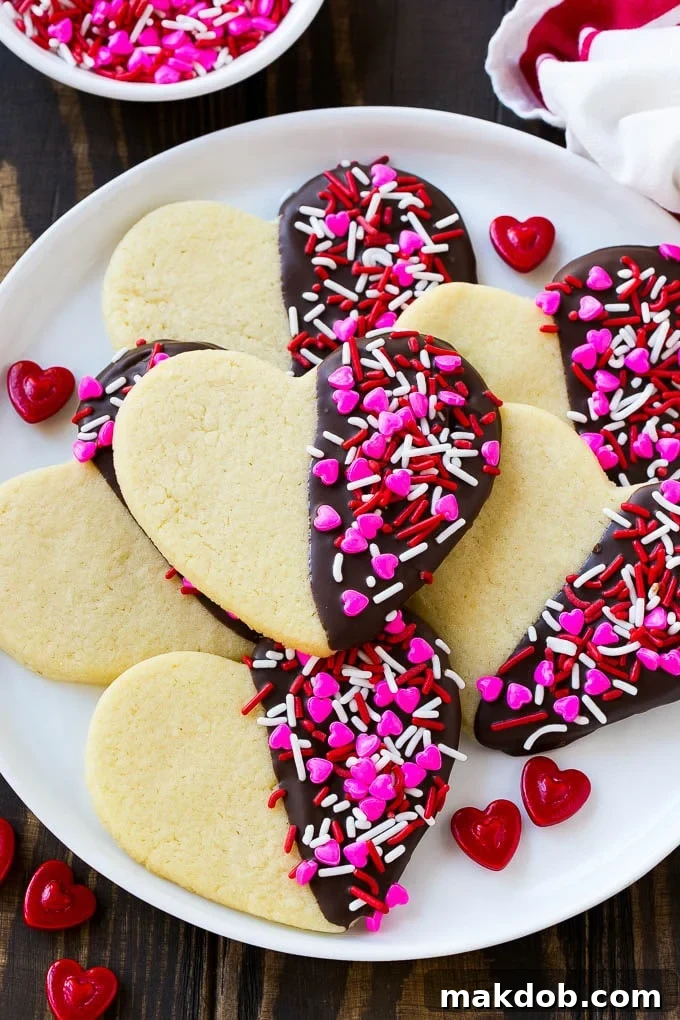 Heart cookies dipped in dark chocolate and decorated with Valentine's Day sprinkles on a white plate with a pink napkin.