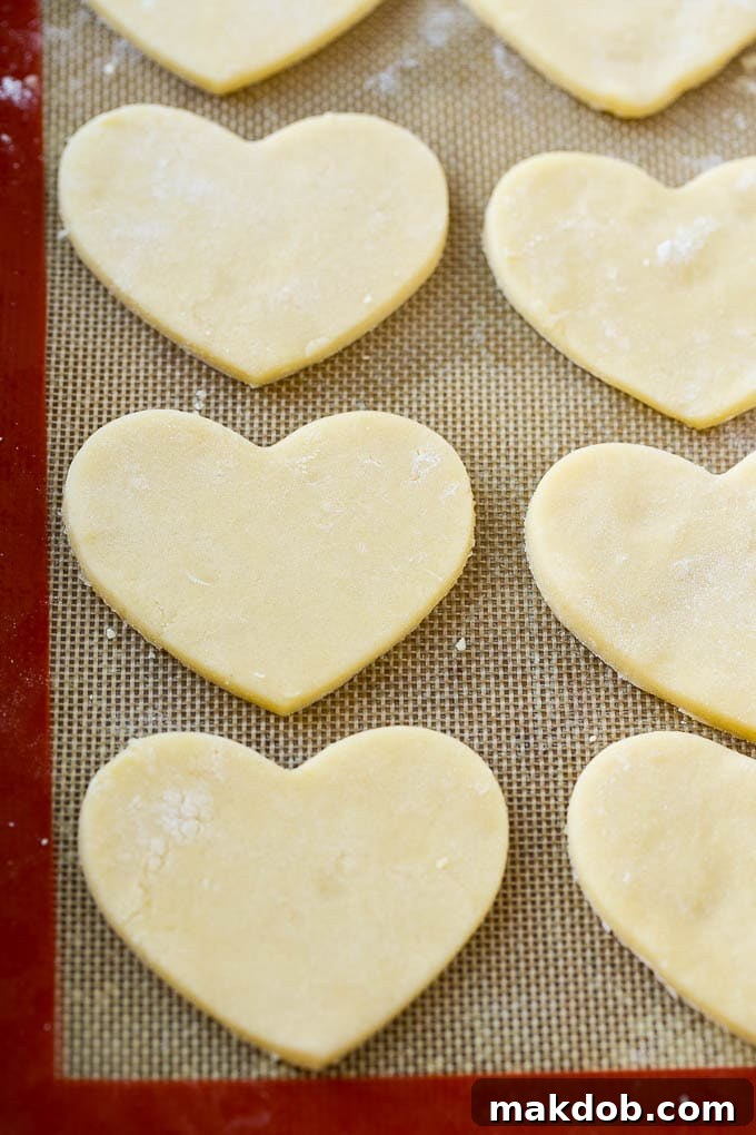 Unbaked heart shaped sugar cookie dough pieces neatly arranged on a baking mat, ready for the oven.