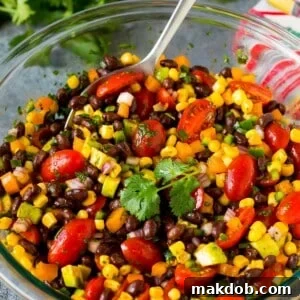 A bowl of black bean salad with a serving spoon in it.