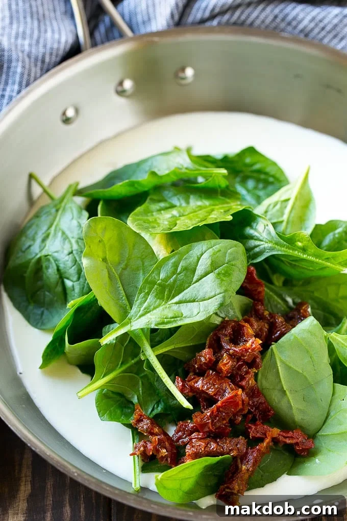 A vibrant, creamy sauce featuring fresh spinach and sun-dried tomatoes bubbling gently in a pan.