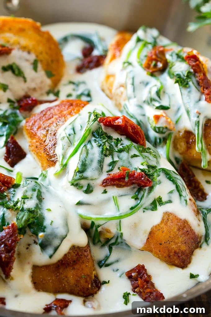 Golden-brown chicken breasts generously topped with creamy spinach and sun-dried tomato sauce in a pan, ready to be served.