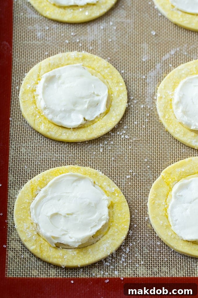 Luscious Fruit Cream Cheese Danish 4 Unbaked puff pastry rounds are shown, each with a creamy, sweet cream cheese filling spread neatly into the scored center, ready for baking.
