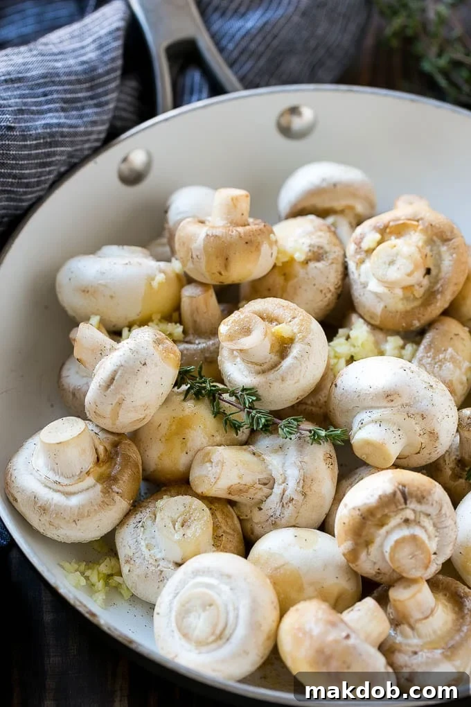 Uncooked buttons with herbs and butter in a frying pan.