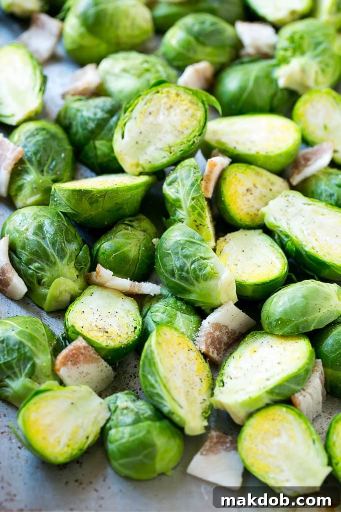 Prepping Brussels Sprouts and Bacon for Roasting Raw halved Brussels sprouts and uncooked chopped bacon on a baking sheet, ready for roasting.