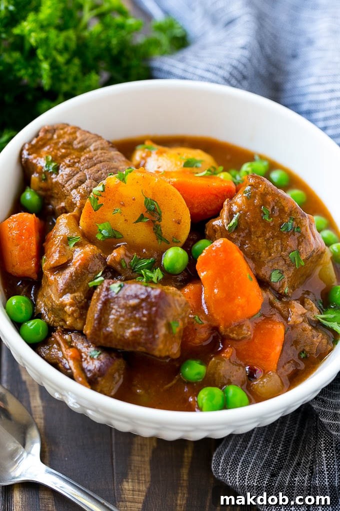 Hearty Slow Cooker Beef Stew 2 A bowl of slow cooker beef stew with meat, carrots, potatoes and peas, garnished with fresh parsley.