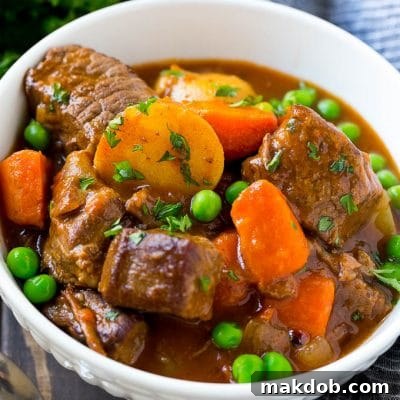 A bowl of slow cooker beef stew with meat, carrots, potatoes and peas.
