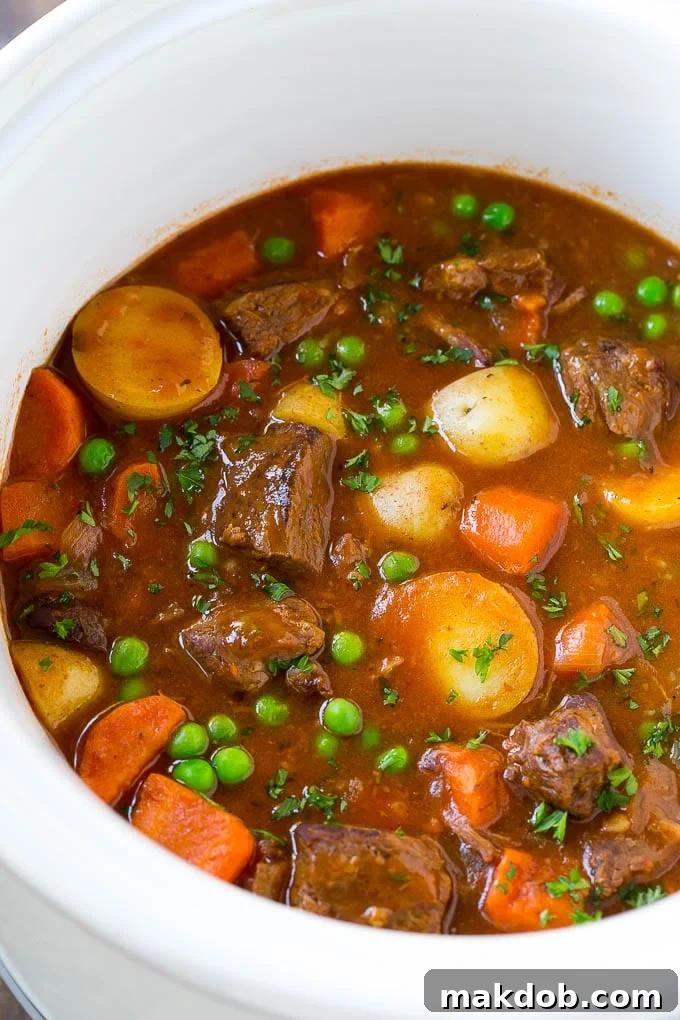 Hearty Slow Cooker Beef Stew 6 A slow cooker filled with a rich and hearty beef stew, showcasing tender meat, potatoes, carrots, and bright green peas.