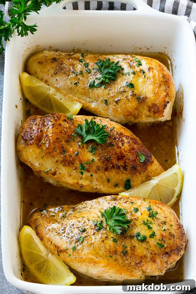 A beautifully arranged baking dish filled with golden-brown baked lemon chicken, glistening with sauce and garnished with fresh lemon slices and parsley.