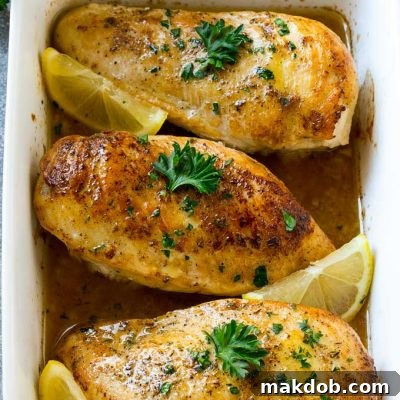 A baking dish full of lemon chicken coated in sauce and garnished with lemons and parsley.
