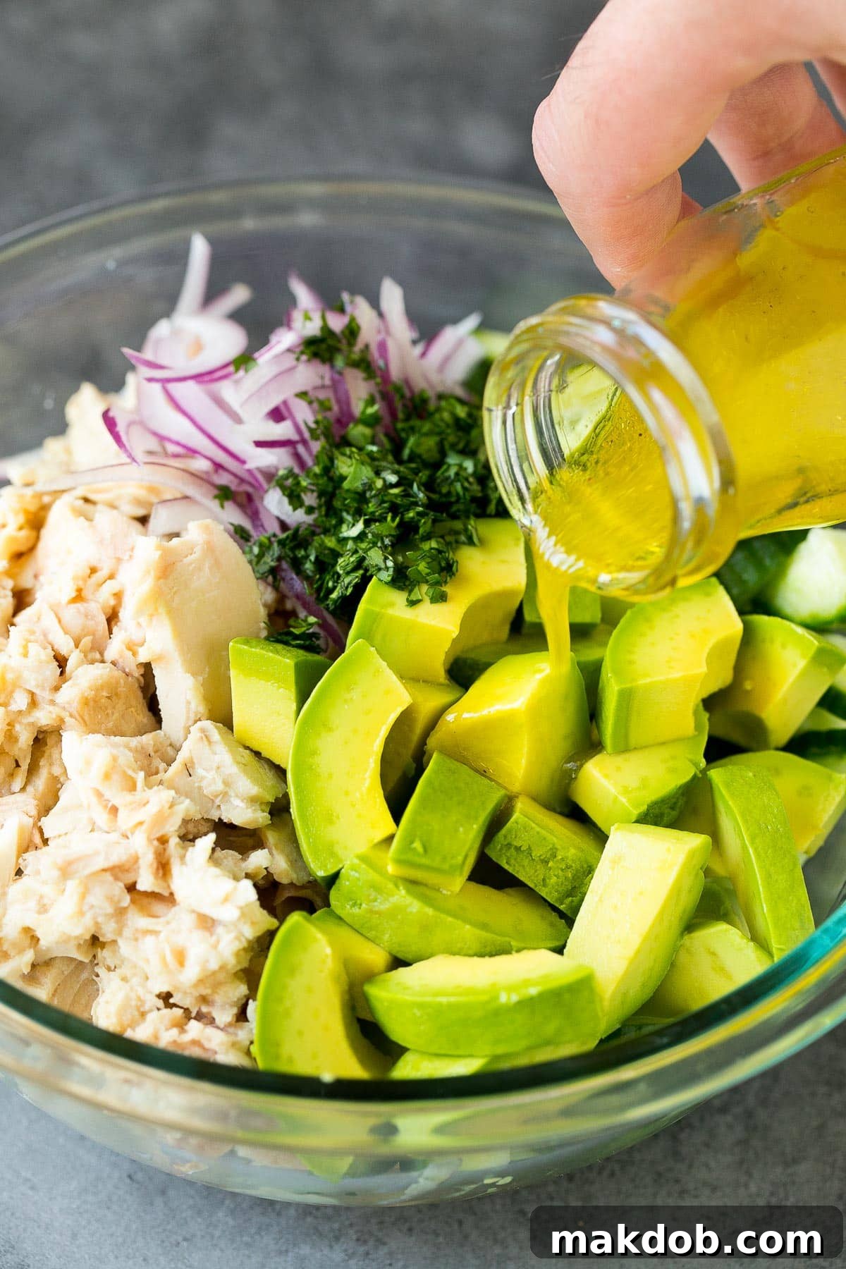A generous pour of the zesty lime dressing flowing into a bowl of prepared tuna salad, ensuring every ingredient is perfectly coated.