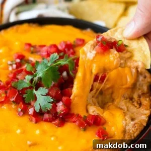 A tortilla chip scooping out a serving of Mexican bean dip.