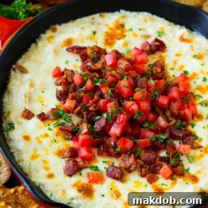 Baked chicken Alfredo dip in a skillet topped with bacon, tomatoes and chopped parsley.