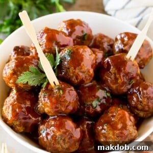 A bowl of grape jelly meatballs served with cocktail forks.