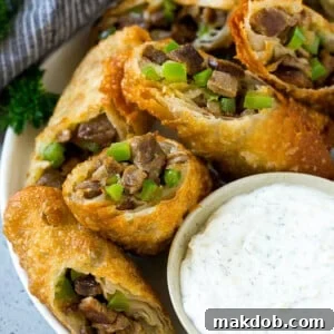 A plate of Philly cheesesteak egg rolls filled with diced steak, peppers, onions and cheese.