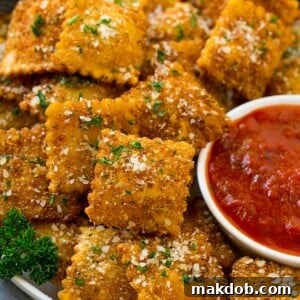 A plate of fried ravioli topped with parmesan and parsley, and served with a side of marinara sauce.