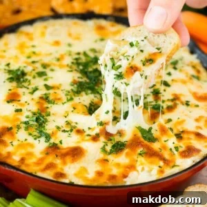 A skillet of artichoke dip with a hand reaching to take a serving.
