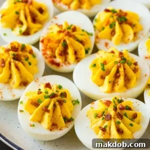 A plate of bacon deviled eggs garnished with sliced chives and smoked paprika.