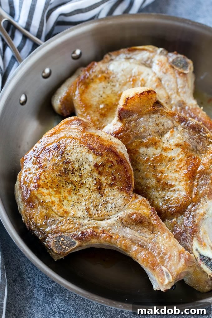 Two browned bone-in pork chops perfectly seared in a cast iron frying pan, ready for the sauce.
