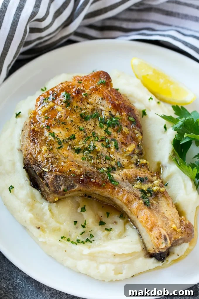 Two glistening brown sugar pork chops arranged beautifully on a bed of creamy mashed potatoes, garnished with fresh herbs.