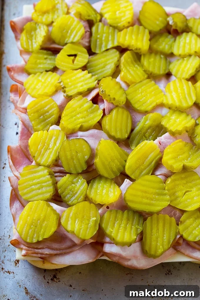 Bread layered with cheese, ham, and pickles, ready for the top bun.