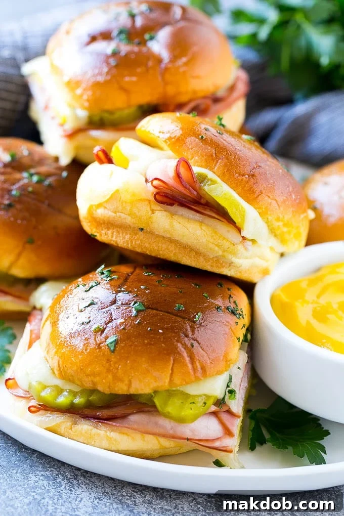 A plate full of golden Cuban sliders with melted cheese, visible pickles, and ham on buns.
