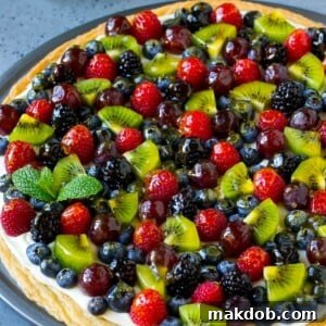 Fruit pizza with a sugar cookie crust and cream cheese frosting, topped with berries, kiwi and grapes.