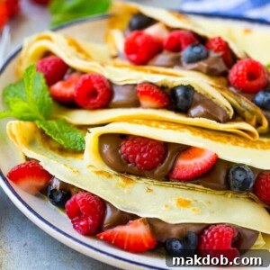 A plate of four crepes that are filled with nutella, strawberries, blueberries and raspberries.