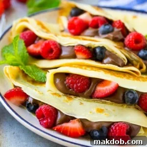 A plate of four crepes that are filled with nutella, strawberries, blueberries and raspberries.