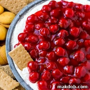 A plate of cherry cheesecake dip with a graham cracker in it.