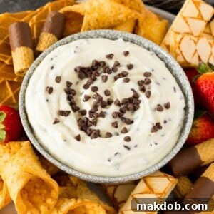 A bowl of cannoli dip surrounded by cookies, cannoli shells and strawberries.