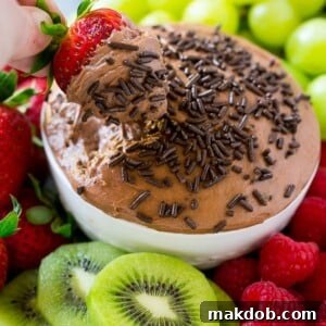 A strawberry in a bowl of chocolate fruit dip, surrounded by assorted fruit.