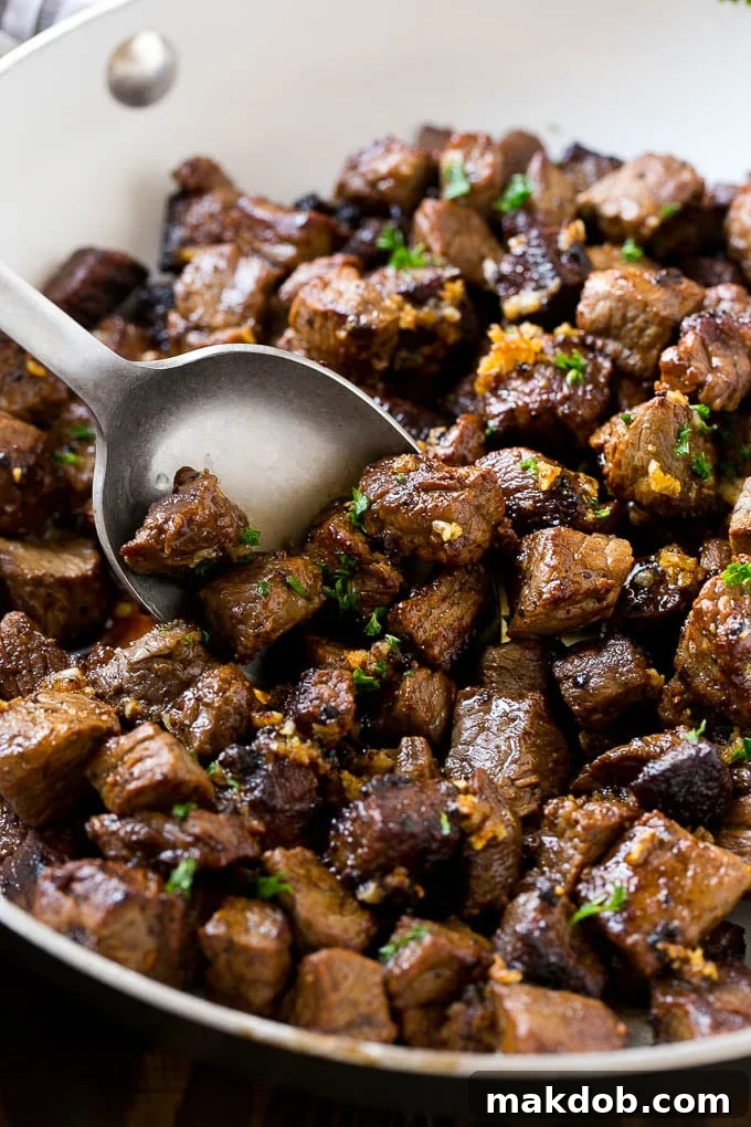 A pan of steak bites with a serving spoon, garnished with fresh parsley.
