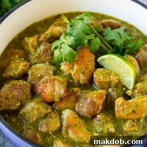 A pot of vibrant green chile verde, garnished with fresh cilantro and lime wedges.