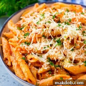 A bowl of penne alla vodka pasta topped with grated Parmesan cheese, fresh parsley, and red pepper flakes.