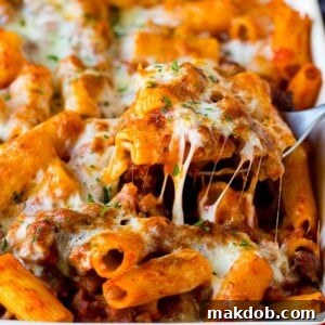 A spoon serving up a portion of Pasta al Forno with rigatoni and sausage.