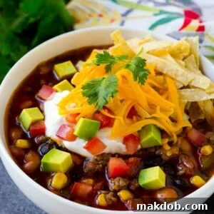 A bowl of taco soup topped with crispy tortilla strips, sour cream, cheese, and fresh avocado.