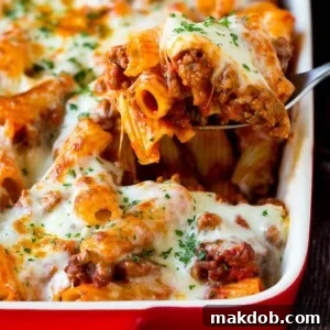 A spoon serving up a portion of baked rigatoni pasta, cheesy and delicious.
