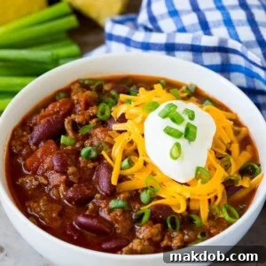 A bowl of beef chili topped with cheese, sour cream, and fresh green onions, ready to be enjoyed.