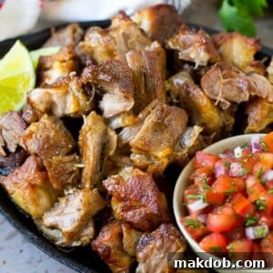 A skillet of crispy pork carnitas served with fresh salsa, ready for tacos.