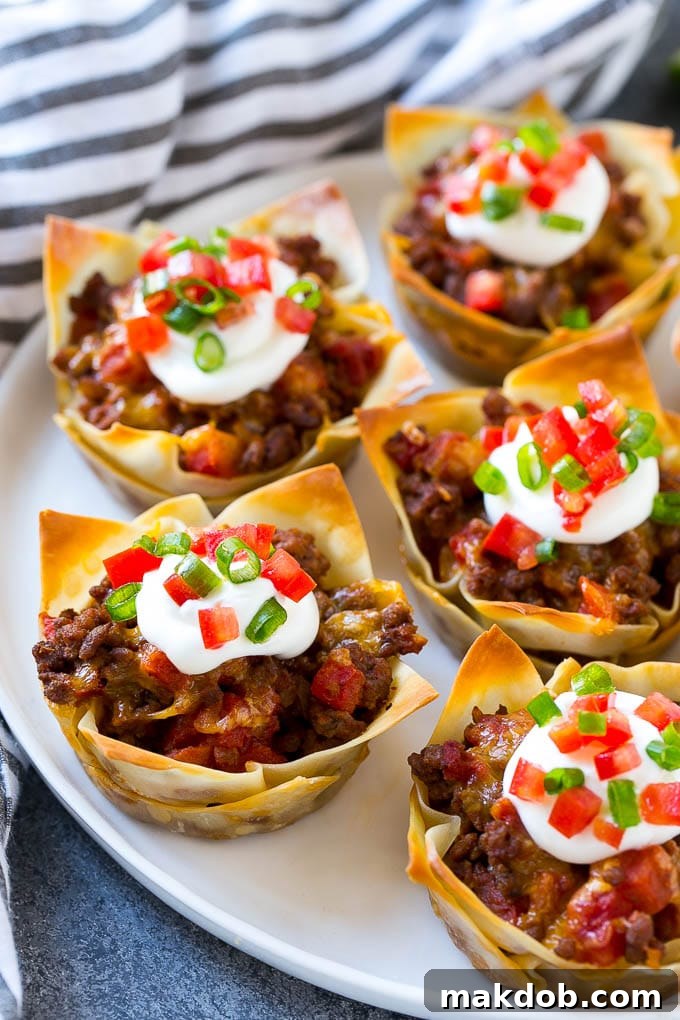 Taco Cups Recipe | Wonton Taco Cups | Taco Cupcakes | Mexican Appetizer #taco #hamburger #appetizer #dinneratthezoo #beef A plate of taco cups made with wontons, seasoned ground beef and cheese, then topped with sour cream, tomatoes and green onions.