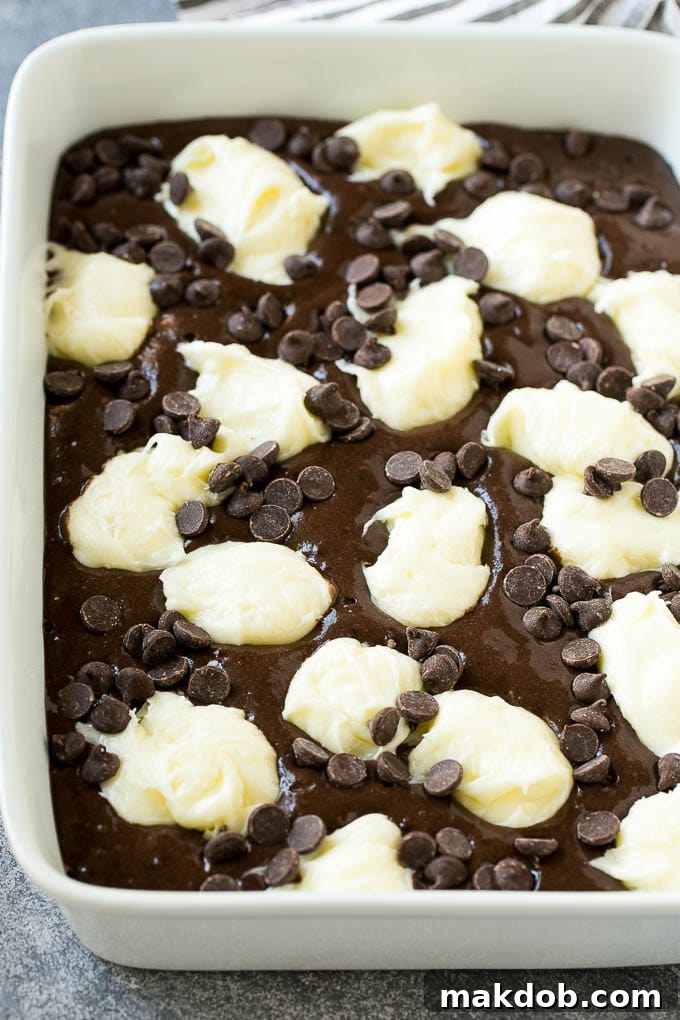 Chocolate cake batter topped with dollops of sweetened cream cheese and chocolate chips, ready for baking.