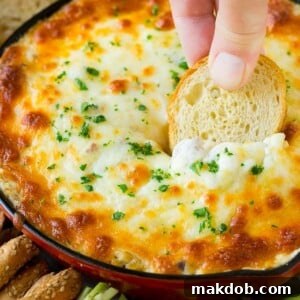A hand expertly scooping a serving of hot, cheesy Reuben dip with a piece of toasted baguette, illustrating its perfect texture and appeal as an appetizer.