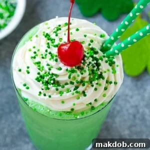 A refreshing mint Shamrock shake, elegantly topped with a generous swirl of whipped cream, colorful sprinkles, and a maraschino cherry for a classic finish.