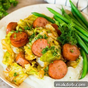 A satisfying plate featuring cabbage and sausage, perfectly served over a bed of creamy mashed potatoes, with a side of fresh green beans for a balanced and hearty meal.