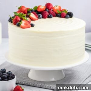 A berry chantilly cake on a cake stand, topped with fresh berries and mint sprigs.