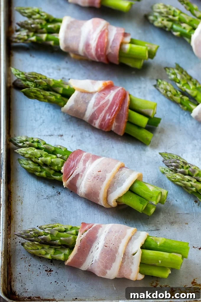 Raw asparagus bundles, expertly wrapped in bacon and coated in glaze, ready for roasting on a sheet pan.