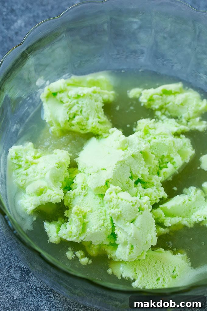 A large bowl containing limeade concentrate and scoops of vibrant green lime sherbet, beginning to be mixed together.