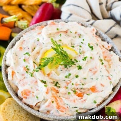 A bowl of rich, creamy smoked salmon dip ready to be served, surrounded by various dipping options like bread and vegetables.