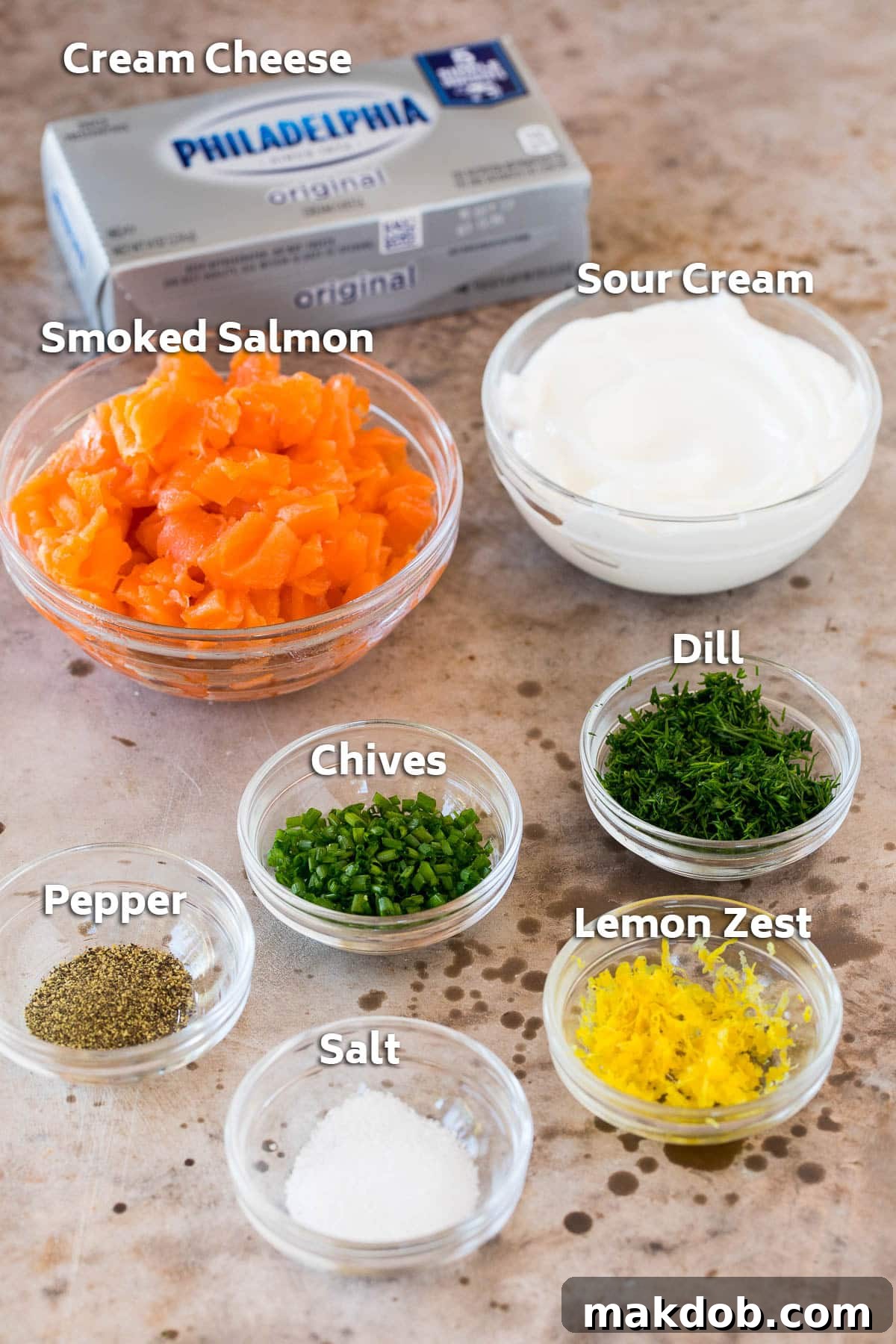 Decadent Smoked Salmon Dip 3 A collection of fresh ingredients laid out on a clean surface, including a block of cream cheese, a tub of sour cream, fresh herbs like dill and chives, lemon, and a package of smoked salmon, ready to be transformed into a delicious dip.